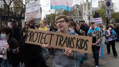 Getty Images Demonstrators pictured in central London in April 2024 protesting against the ban on puberty blockers. A sign held by a demonstrator in the middle of the shot reads "protect trans kids". 
