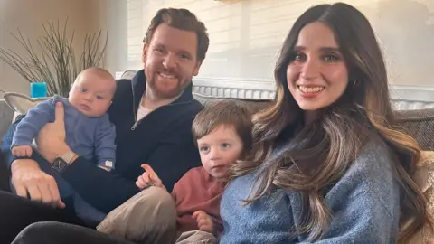 Paul Gorton, Kate Waldron, and their children Charlie and Cooper sit on the sofa. 
