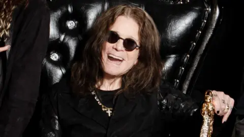 Ozzy Osbourne smiling, seated on a black leather throne