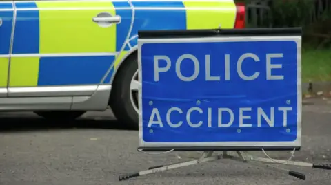 A blue police accident sign in front of the back wheel of a police car.