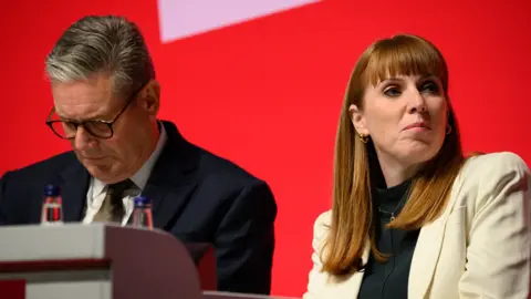 Getty Images Sir Keir Starmer and Angela Rayner sit next to each other in front of a bright red background.