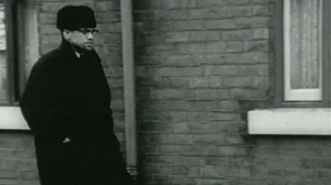 Malcolm X walks down a street in Smethwick.