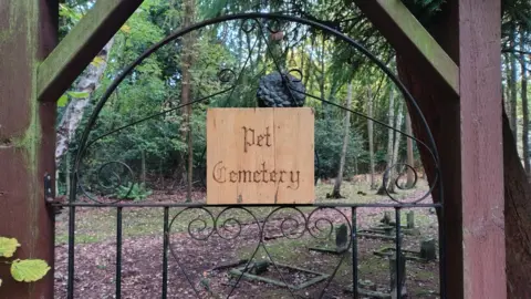 A black gate with a wooden sign saying 'Pet Cemetery'. 