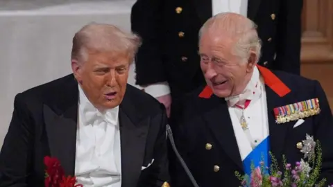 King Charles and US President Donald Trump are sat next to one another at a formal banquet. 