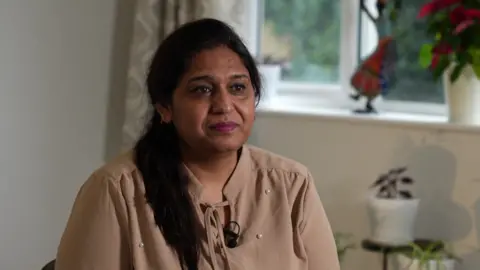 Seema Misra in a brown chiffon top sitting in her living room