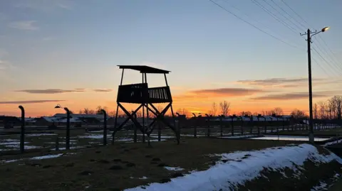 An evening view of Birkenau and a Nazi watchtower as snow lies on the ground