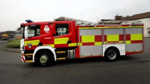 A slightly blurred image, showing motion, of a Cleveland fire engine turning a corner on a residential street. The vehicle is red and yellow with ladders on top.