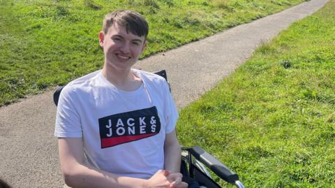Jack in a wheelchair in a park smiling at the camera