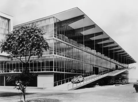 Getty Images A black and white image of Dusseldorf's Hanielgarage, showing its sleek lines and glass structure with a VW Beetle being driven down a ramp 