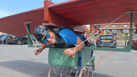 Chloe Juyon A man smiles as he crouches down in his home-made creation, which is a pair of wings on top of a pram-type structure, which will be entered in the Birdman Bristol competition.