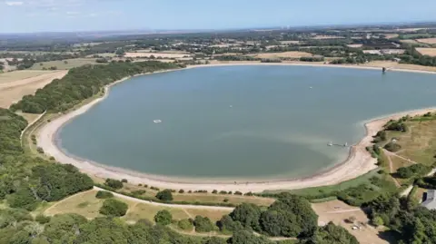 BBC / Ben Leete An aerial view of a reservoir. The water is blue and there is a brown margin around the lake where the water has receded. The fields around the edge are varying shades of brown and pale green.