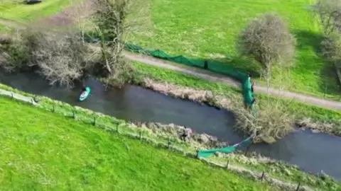 Aerial of river bank and fields in Twyford, Hampshire with green netting across the water.
