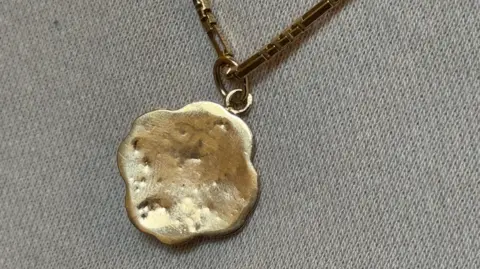 The reverse of a gold pendant is shown with gold bite marks in it. It is shaped in the leaf of an Edelweiss flower.