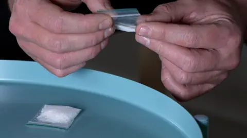Getty Images A man's hands hold a bag of ketamine while another bag rests on the table in front of him.