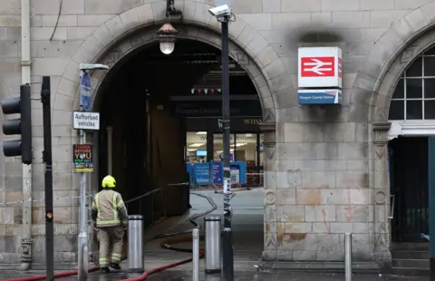 PA Media A firefighter by an entrance to the closed Glasgow Central railway station as work continues to dampen down the remains of a fire which broke out in a building adjacent to the railway station.