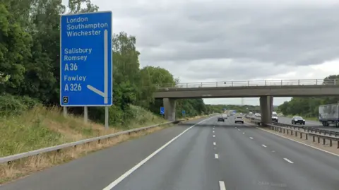 Eastbound carriageway of M27 with a blue sign for junction 2. The road has several cars on it.