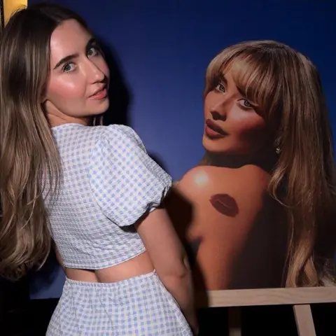 Sabrina Carpenter fan Amy posing alongside a poster of the star