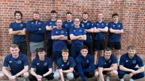 Sedgefield Water Polo Club The full water polo team posed in front of a brick wall with a row crouched down in front of a row standing up.