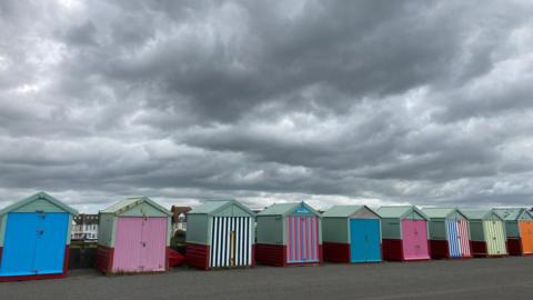 A row of colourful beach huts on a promenade below threatening grey clouds