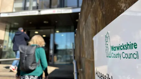 Image of people walking into the entrance of Shire Hall, Warwick. A lady in a green coat ascends stairs.
