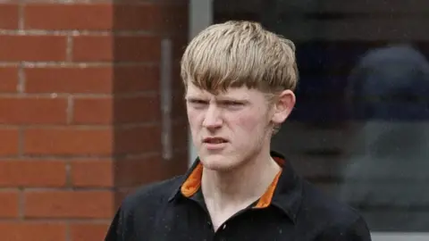 Isaac Adams, with fair hair, dressed in a black and orange shirt.
