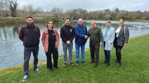 Angling Trust Seven people by a body of water. Two men in the middle are shaking hands.