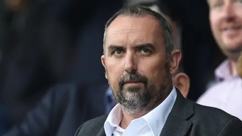 Getty Images A close-up photo of Kelvin Thomas. He is looking off camera, and wearing a white shirt and black jacket.