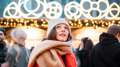 Getty Images A woman with a white hat brown hair and red and brown scarf.