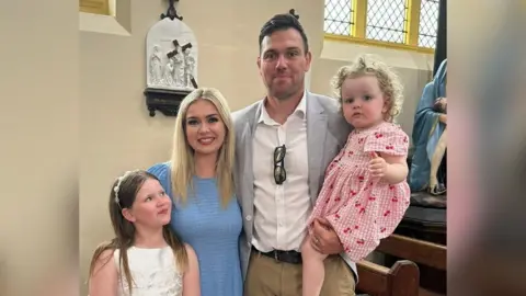 Family handout Glen stands with his wife and two children in a church. They are dressed as wedding guests, and are smiling at the camera. Their oldest daughter is looking and smiling at Amber.