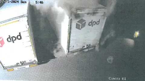 Police handout CCTV still of the rear of two DPD lorries - smoke is coming out of the rear of the lorry on the right hand side.