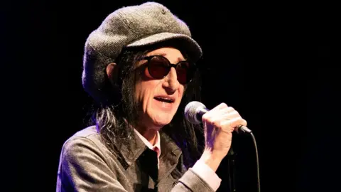 Getty Images John Cooper Clarke talking into a microphone on stage