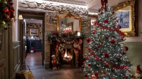 Kirsty Anderson A fireplace and decorated Christmas tree adorned with decorations