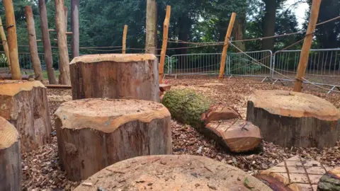 Wooden play area with rounded tree stumps, cross-etched logs and bark chippings all over the ground