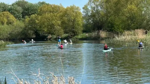 Charlotte Westcott Eight kayaks with one person in each of them - guiding along the river. 