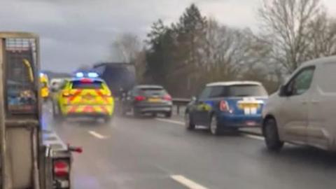 An emergency vehicle driving between two lanes of queuing traffic in heavy rain on a carriageway