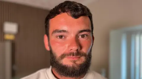 Will Griffiths has brown hair, eyes and a beard. He is looking directly at the camera
