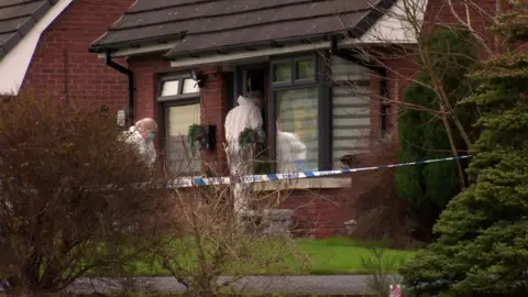 Forensic officers wearing white suits and face masks enter a house