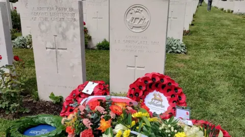 Crown Copyright Commonwealth war grave headstones, including one for J.E. Springate, with poppy wreaths and flowers placed in front.