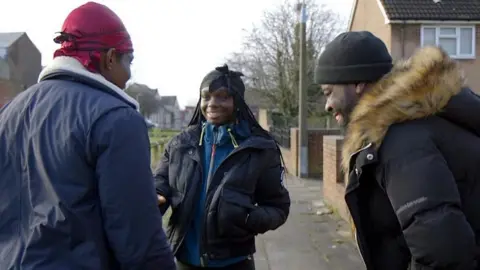 Three people talk and laugh in street