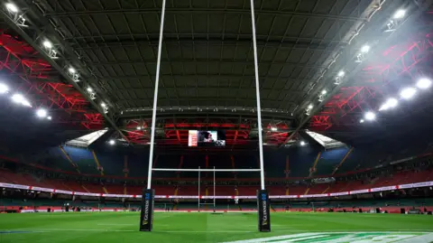 Principality Stadium from behind one of the goalposts. Red strobe lights flicker near the roog of the stadium.