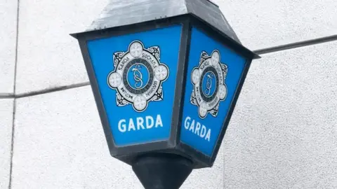 Generic picture of a Garda sign in blue and white, close up of the force badge in celtic style, white text on blue background 'Garda'