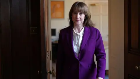 PA Media Rachel Reeves walking through a doorway at 11 Downing Street. She is wearing a purple trouser suit and white shirt.