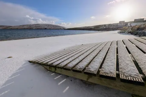 Jeannie/BBC Weather Watchers Snow dusts a duck board path and a beach in Shetland.