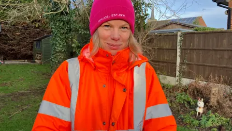 Anna Alls, dressed in a hi-vis jacket and wooly hat, looking at the camera