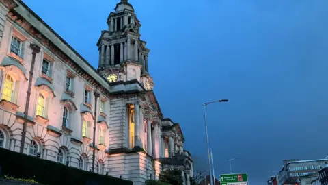 Stockport town hall, as taken from below and at night, when the windows are lit from underneath. It is a large white stone building.