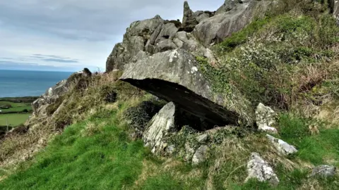 Prof George Nash A flat capstone supported be a single upright overlooking the sea.