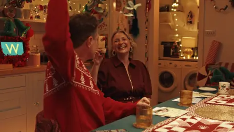 Waitrose Joanna Page laughs as she holds a mince pie, next to Matthew Horne who wears a red Christmas jumper