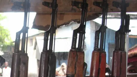 Someone starring into a market stall selling automatic weapons in Mogadishu in 2006