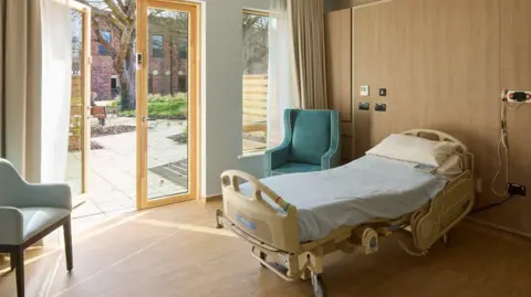 Moya Cole Interior shot of hospice room with bed, and veranda door which opens onto the courtyard.