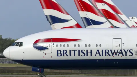 Stock image of a British Airways plane on a runway, with the tail fins of other BA planes visible in the background.